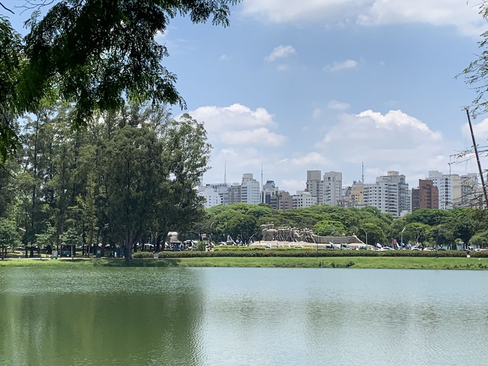 Lago do Parque Ibirapuera com o Monumento às Bandeiras e os prédios de Moema ao fundo, em dia de céu azul